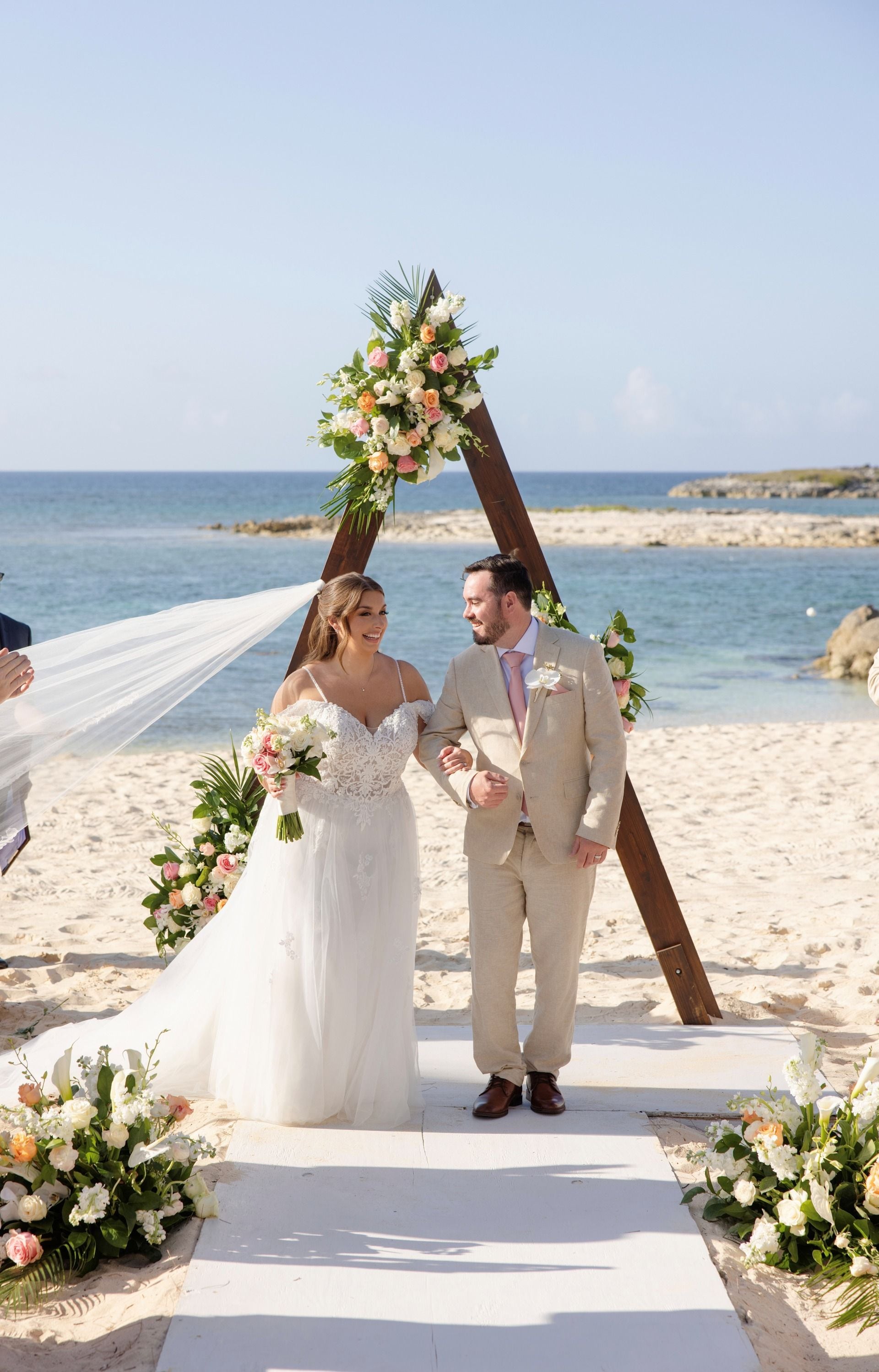 Bride and groom exiting wedding ceremony under floral arch on beach
