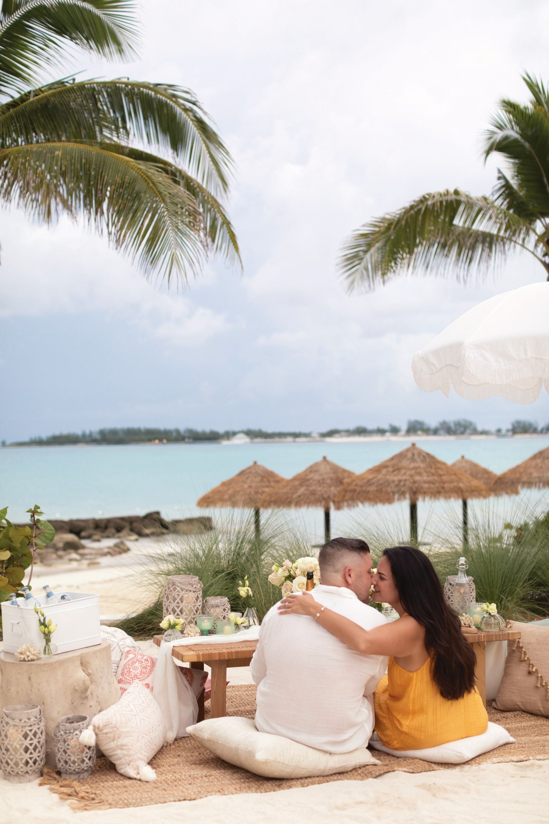 Romantic beach picnic proposal setup with pillows, flowers and ocean views at Sandals Resort