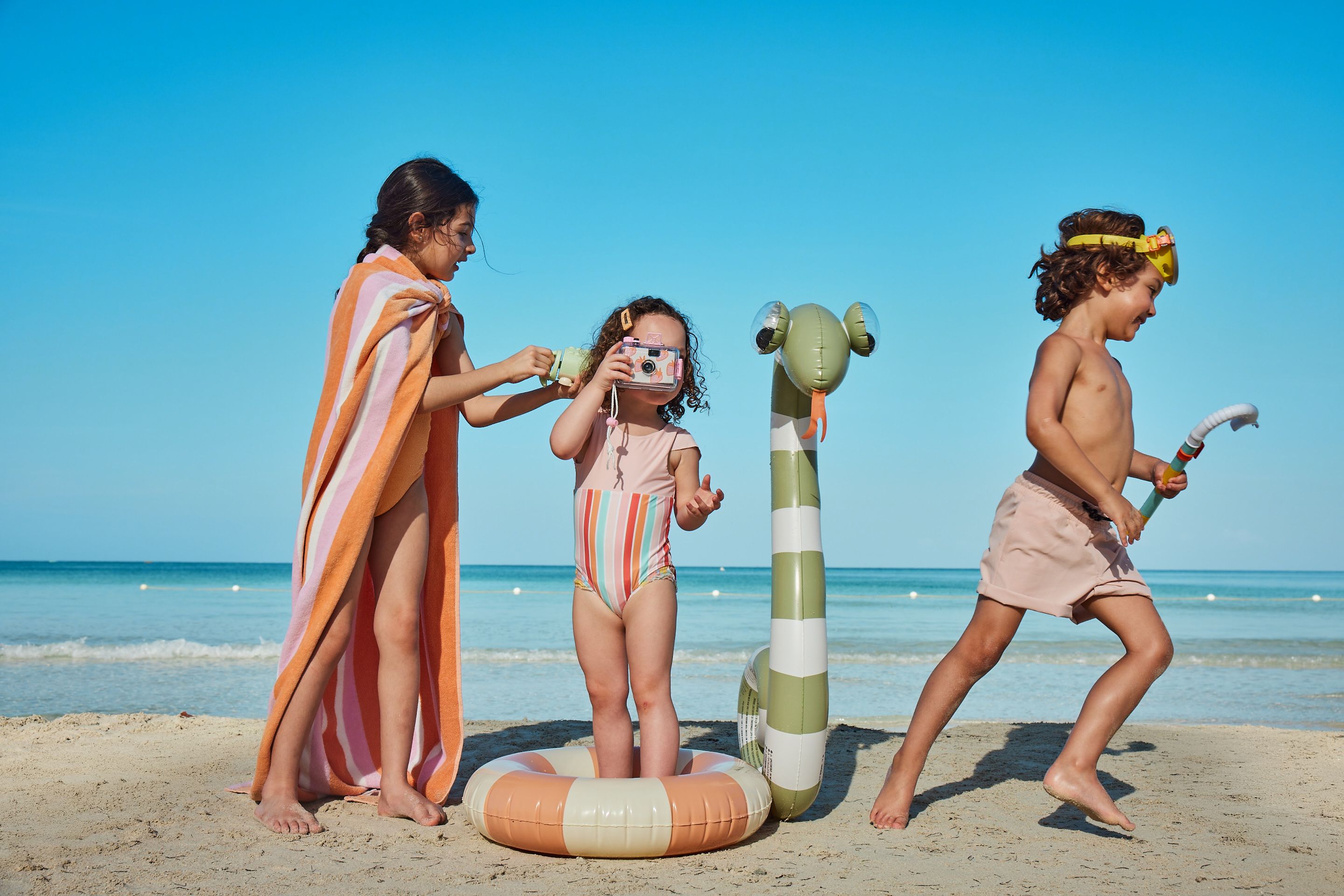 Three children playing on a beach with inflatable toys near the shoreline.